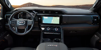GMC truck dashboard interior with touchscreen display, steering wheel, and desert landscape visible through windshield at sunset