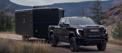 Black GMC pickup truck towing enclosed cargo trailer in mountain landscape
