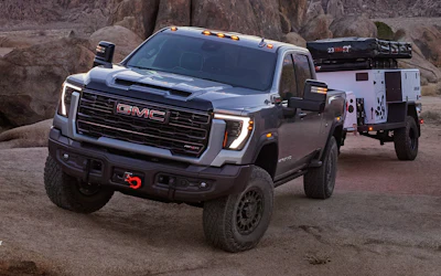 Silver GMC Sierra truck with custom front bumper towing white service trailer in rocky desert landscape