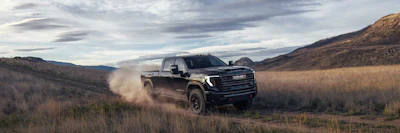 Black GMC Sierra pickup truck driving through dusty desert terrain with mountains in background