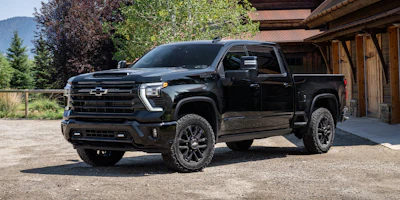 Black Chevrolet Silverado HD pickup truck parked in front of wooden garage with mountains in background