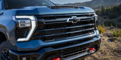 Blue Chevrolet pickup truck front grille and headlights with mountainous landscape background