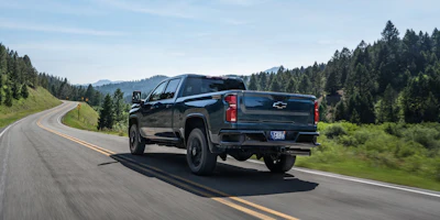 Blue Chevrolet Silverado pickup truck driving on a curved mountain highway surrounded by evergreen forests