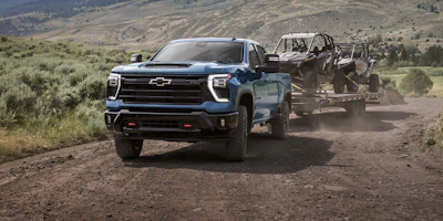 Blue Chevrolet Silverado truck towing trailers on a dusty mountain road with sagebrush landscape