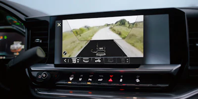 Vehicle infotainment display showing 360-degree camera view with road ahead and parking guidance overlay