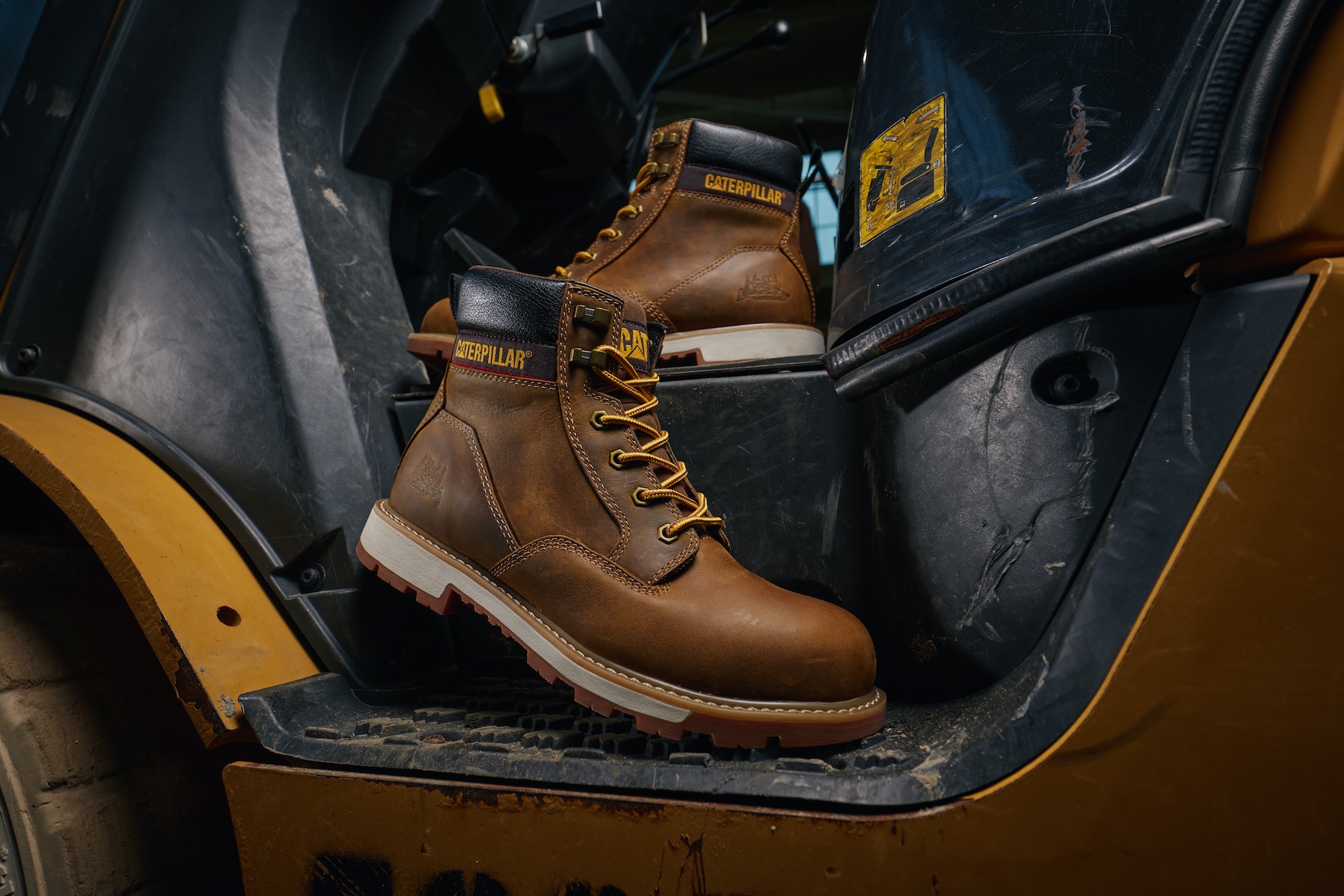 Brown leather Caterpillar work boot with yellow laces displayed in yellow vehicle interior