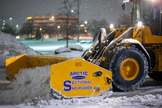 Yellow snow plow with Arctic Sectional Snow-Pusher attachment clearing snow from urban street at night