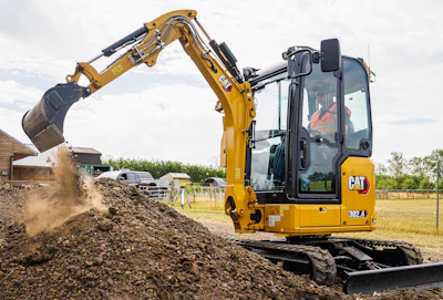 Yellow CAT 382.4 excavator dumping soil at a construction site with operator visible in cab