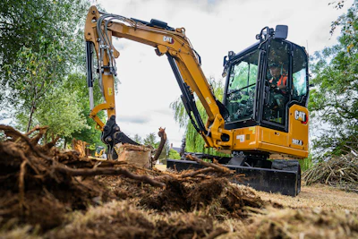 Yellow Caterpillar 302.6 mini excavator digging soil at a construction site surrounded by trees
