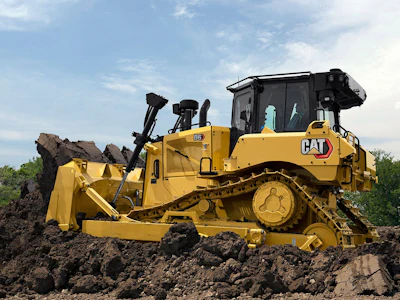 Yellow Caterpillar D6 bulldozer pushing large pile of dark soil and rocks on construction site