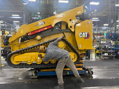 Technician performing maintenance on yellow Caterpillar 243 skid steer loader in factory setting