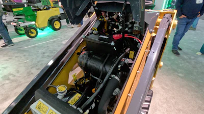 Open engine compartment of yellow and black heavy equipment with mechanical components visible at industrial trade show