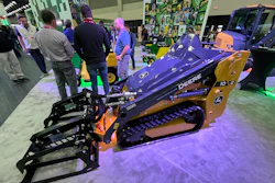 Purple and gold John Deere compact track loader on display at an indoor equipment exhibition with visitors