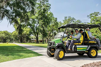 Custom green and yellow golf cart with passengers driving through a tree-lined park pathway on a sunny day