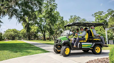 Custom green and yellow golf cart with passengers driving through a tree-lined park pathway on a sunny day