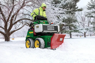 Worker operating green John Deere snow plow with Western brand equipment clearing snow from park pathway in winter