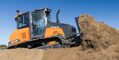 Orange and black Develon DD130 bulldozer working on sandy terrain under clear blue sky