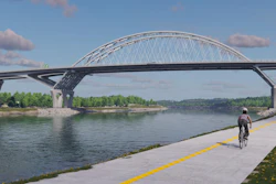 Modern bridge with arched design spanning river, featuring dedicated yellow-lined cycling path alongside, with trees and blue sky in background