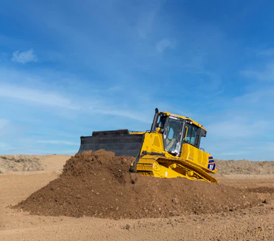 Yellow komatsu DX61PXi bulldozer pushing soil at a construction site under clear blue sky