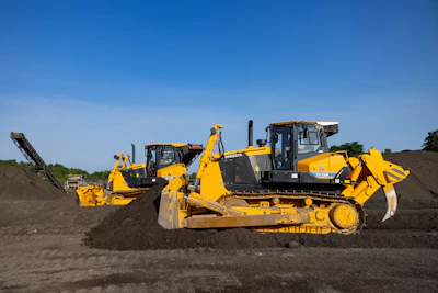 Yellow Dressta TD-15M and TD-25M bulldozers operating on a dirt construction site under clear blue sky