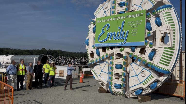 Tunnel boring machine with Emily Clean Rivers Project branding at construction site with workers