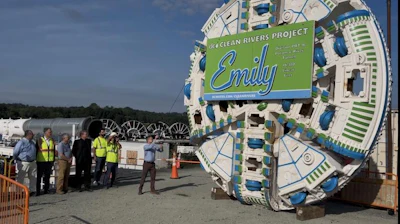 Tunnel boring machine with Emily Clean Rivers Project branding at construction site with workers