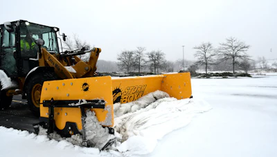 Yellow snow plow attached to heavy equipment clearing snow from a frozen waterway in winter conditions