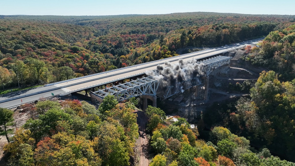 Highway bridge crossing forested valley with river below during autumn season