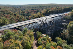 Highway bridge crossing forested valley with river below during autumn season