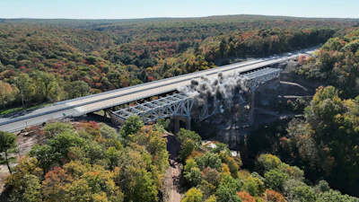 Highway bridge crossing forested valley with river below during autumn season