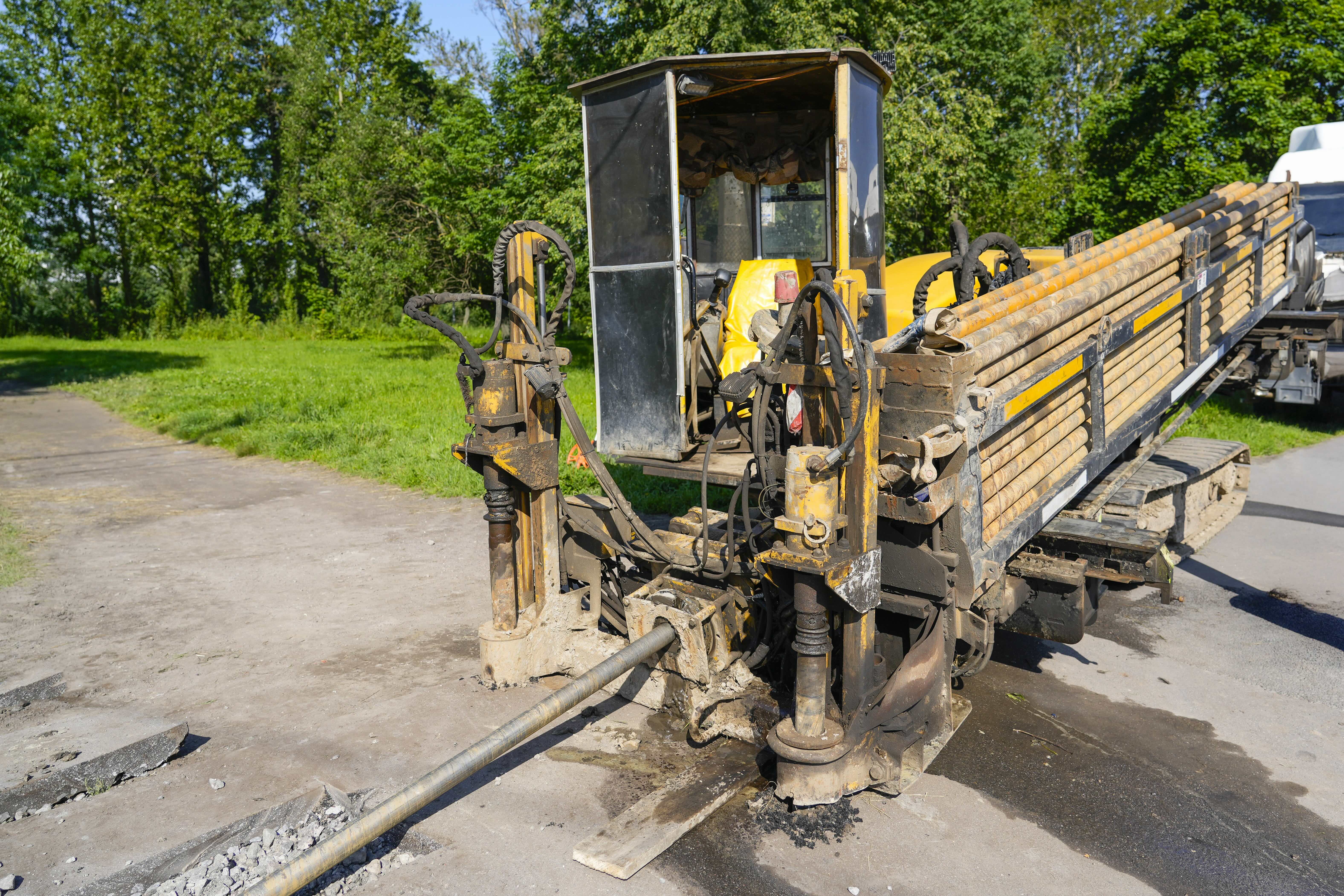 Yellow and black horizontal directional drill on asphalt road with wooden trailer and green trees in background