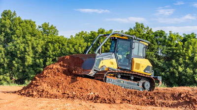Yellow and black Hyundai HD130 bulldozer pushing large pile of reddish-brown soil on construction site surrounded by trees