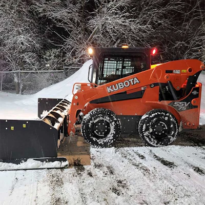 Orange Kubota skid steer loader clearing snow at night with headlights on