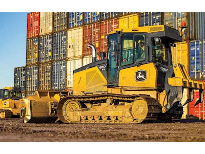 Yellow John Deere 650 P-Tier bulldozer with tracked treads positioned in front of stacked shipping containers at a logistics yard