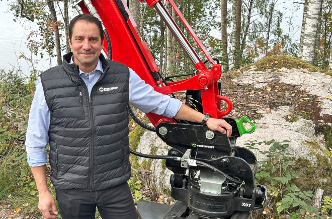 Man in Weidemann vest posing with red X07 wheel loader in forest setting