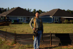Construction worker Leo Vanegas in tool belt standing before new residential homes under development