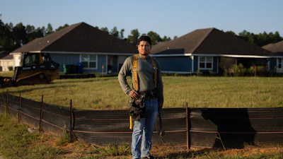 Construction worker Leo Vanegas in tool belt standing before new residential homes under development