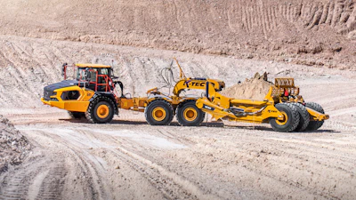 Yellow K-Tec 1232 ADT scraper being pulled by Komatsu articulated dump truck chassis on dirt road in quarry