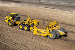 Yellow K-Tec 1232 ADT scraper being pulled by Komatsu articulated dump truck chassis on unpaved construction site