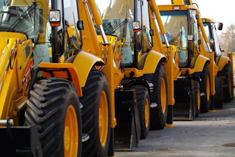 Row of yellow and black heavy construction wheel loaders parked in line at an equipment yard