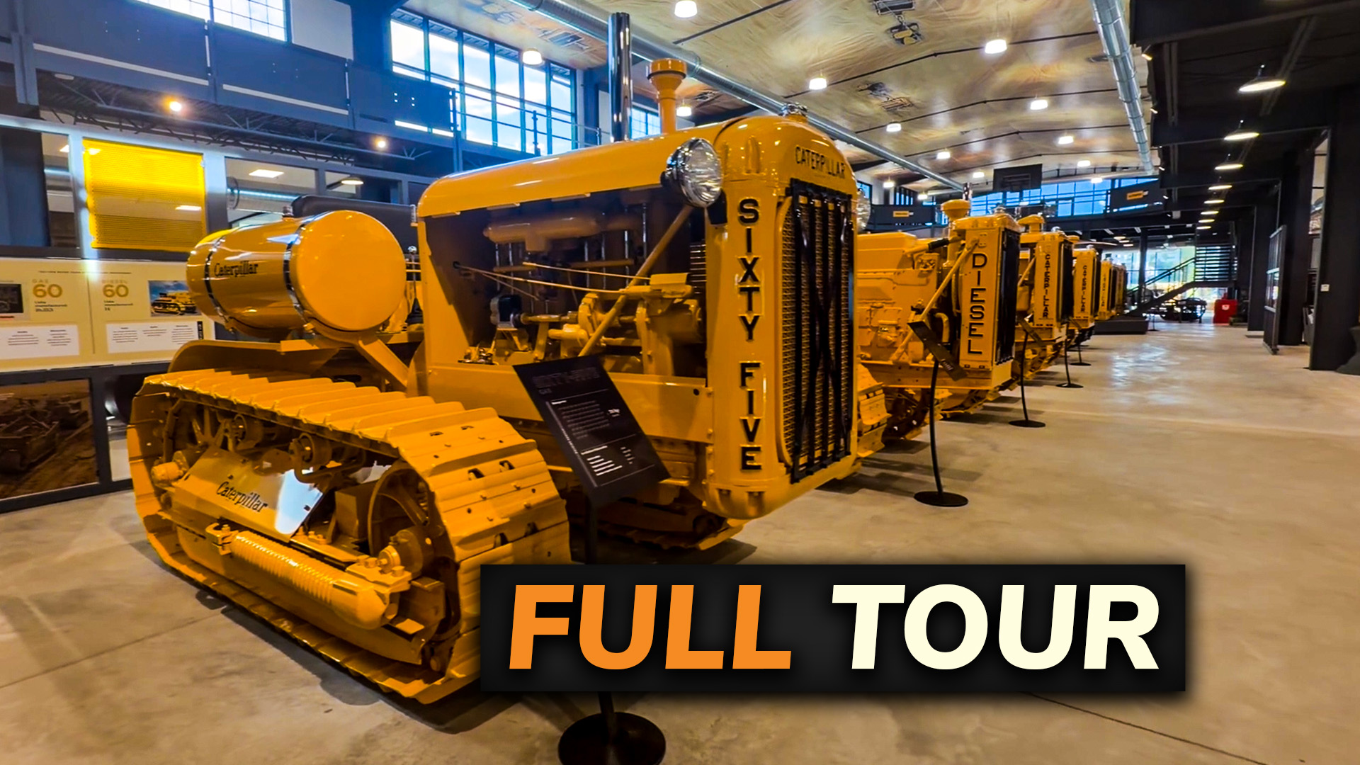 Row of yellow Caterpillar construction equipment displayed in an indoor museum or exhibition space with full tour signage
