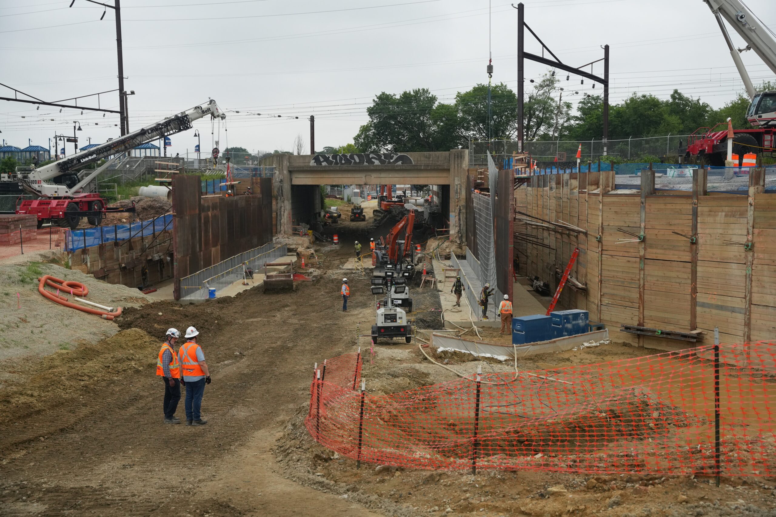 Construction site with workers in safety gear operating machinery within wooden barriers and protective fencing