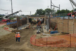 Construction site with workers in safety gear operating machinery within wooden barriers and protective fencing