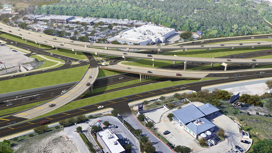 Aerial view of a complex highway interchange with multiple elevated roadways, overpasses, and surrounding commercial buildings and green spaces.