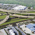 Aerial view of a complex highway interchange with multiple elevated roadways, overpasses, and surrounding commercial buildings and green spaces.