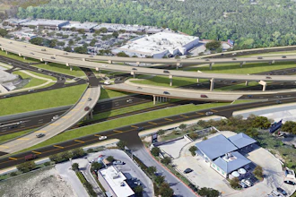 Aerial view of a complex highway interchange with multiple elevated roadways, overpasses, and surrounding commercial buildings and green spaces.