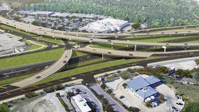 Aerial view of a complex highway interchange with multiple elevated roadways, overpasses, and surrounding commercial buildings and green spaces.