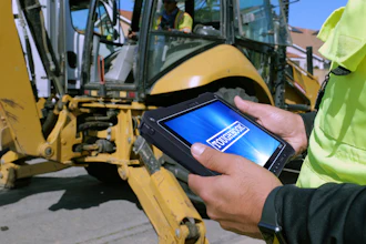 Construction worker holding Panasonic Toughbook G3 tablet with blue screen display near yellow backhoe on jobsite