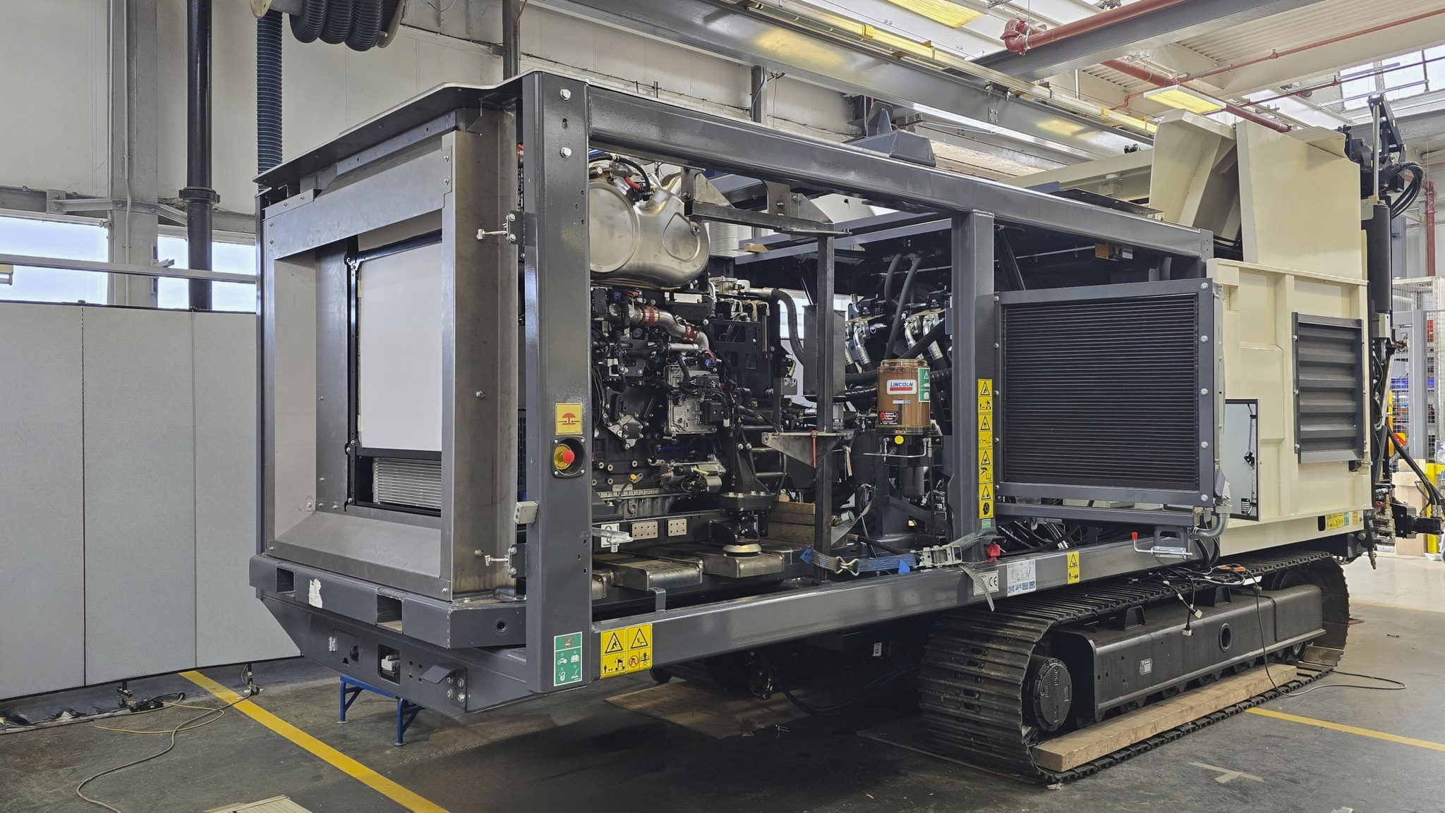 Mobile diesel generator unit with engine exposed, mounted on tracked platform in industrial warehouse facility