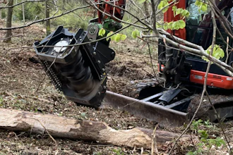 Heavy forestry equipment with grapple bucket attachment sorting logs in wooded area